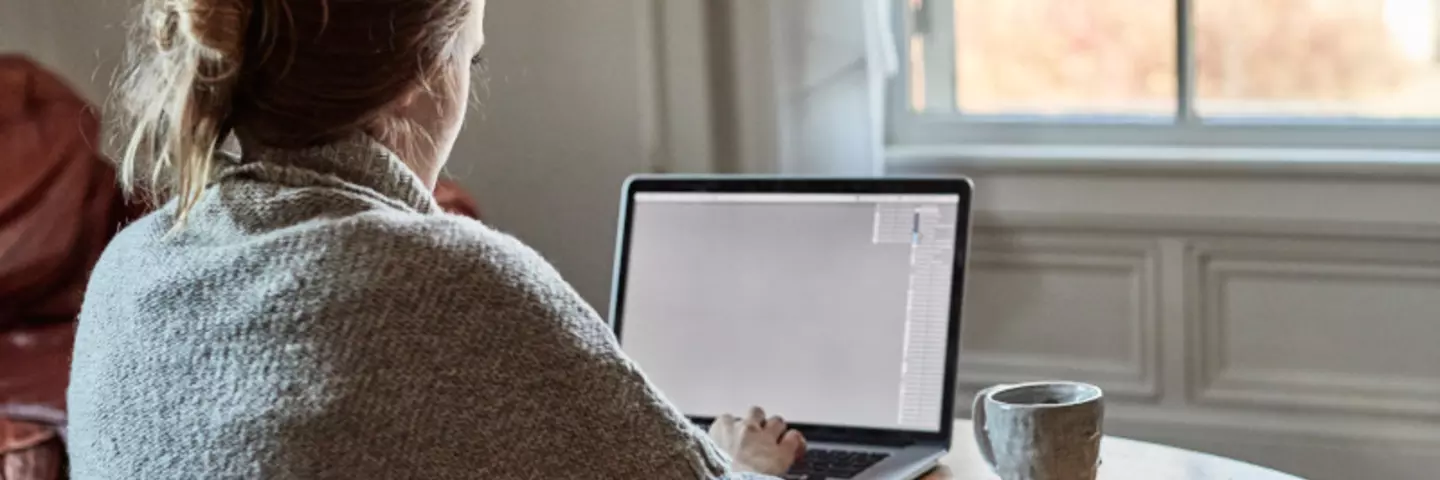 Frau sitzt am Laptop mit einer Tasse daneben
