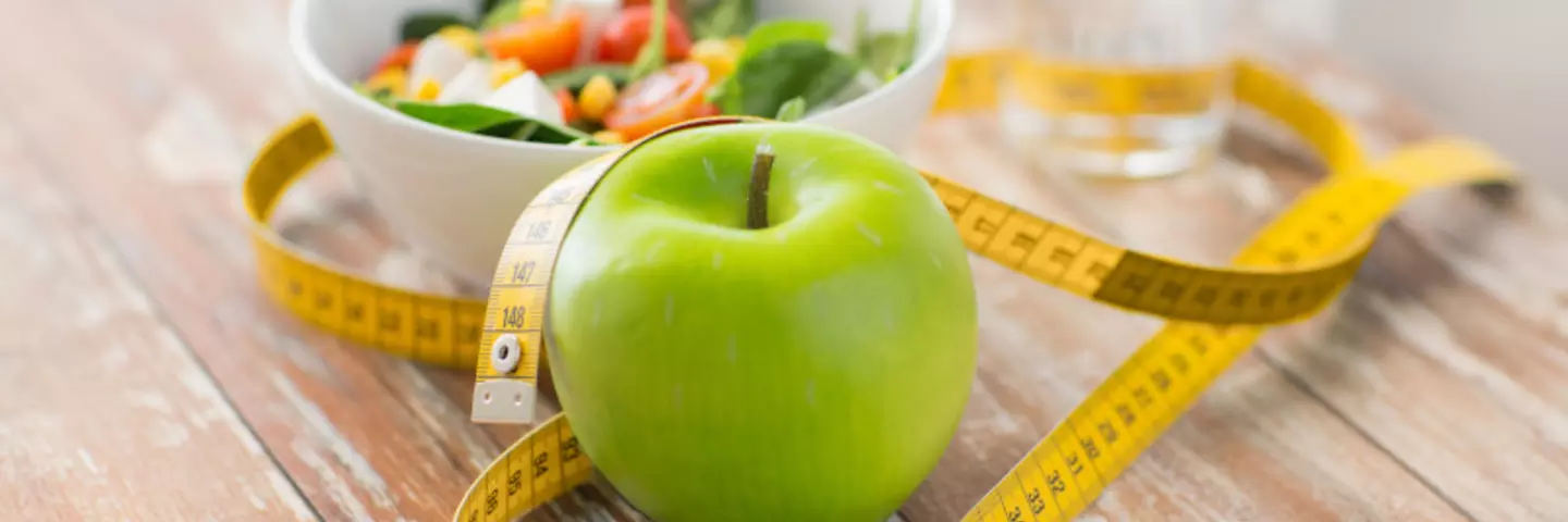 Maßband um einen Apfel und eine Schüssel Salat gewickelt