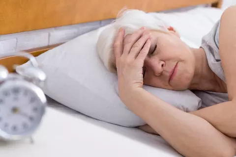 Frau mittleren Alters liegt schlaflos im Bett